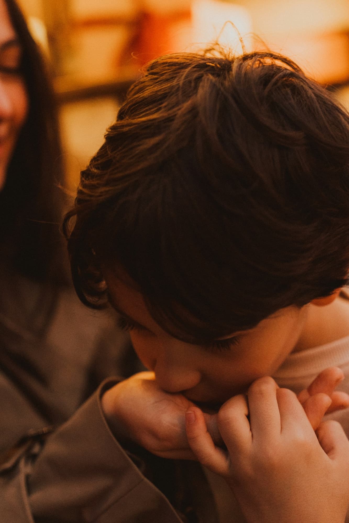 Young boy with head down, hands clasped, in warm indoor light