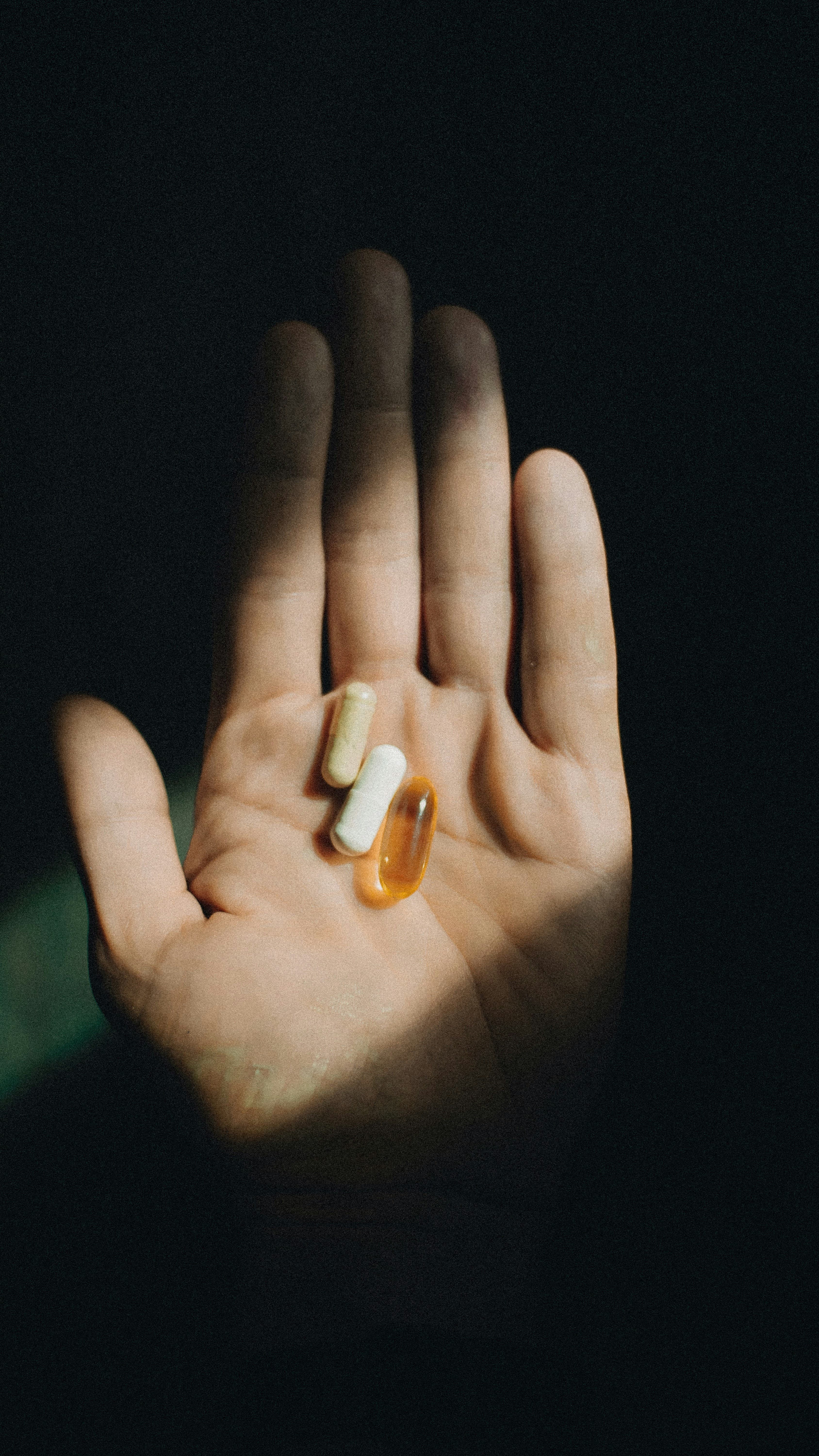 Hand holding a few capsules against a dark background