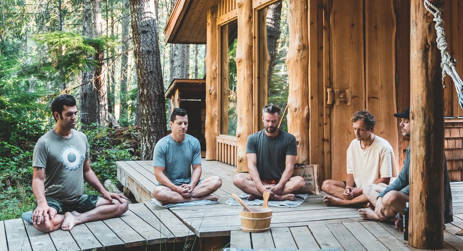 Men sitting in meditation on a forest cabin deck
