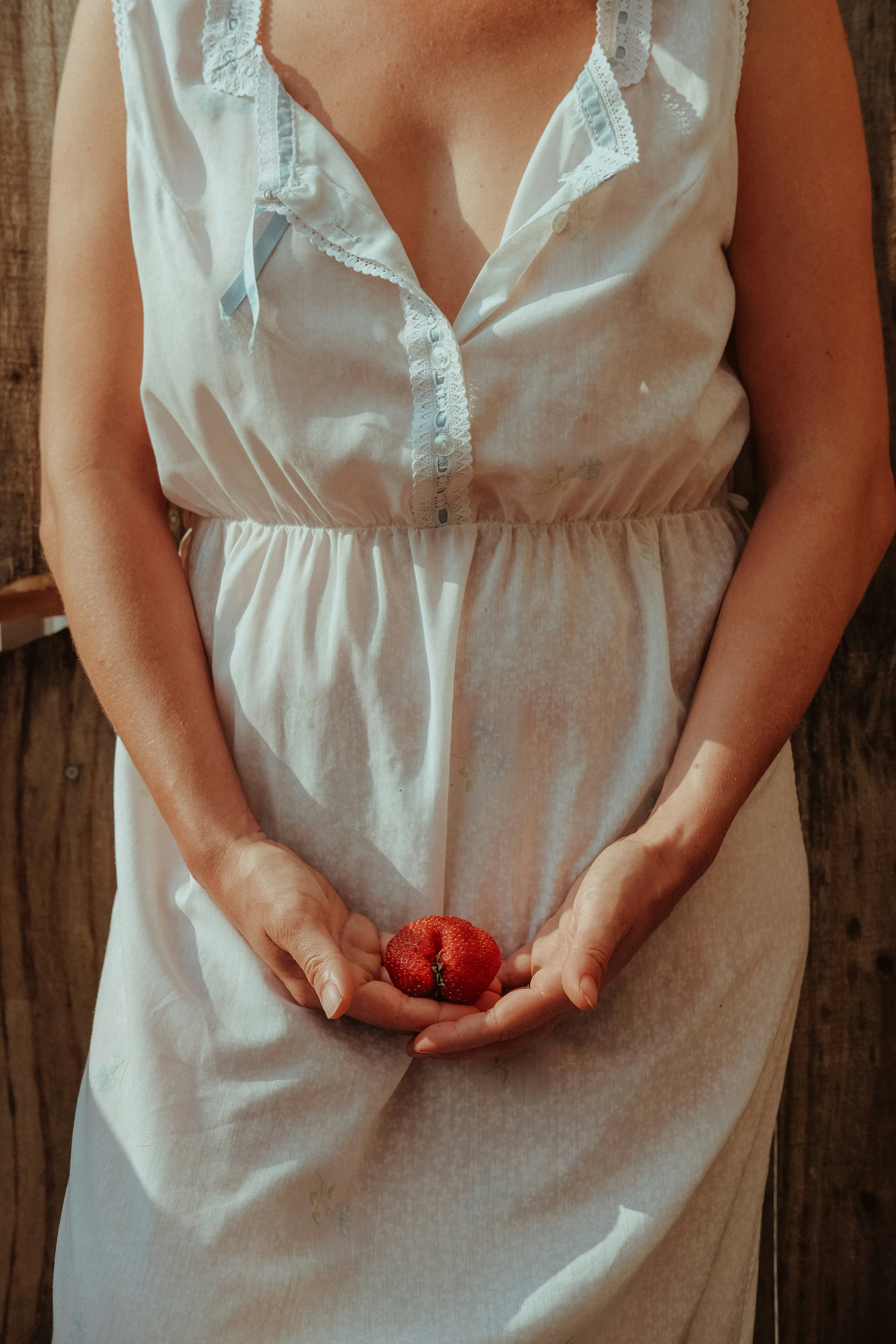 Woman in a soft white dress holding a strawberry in cupped hands
