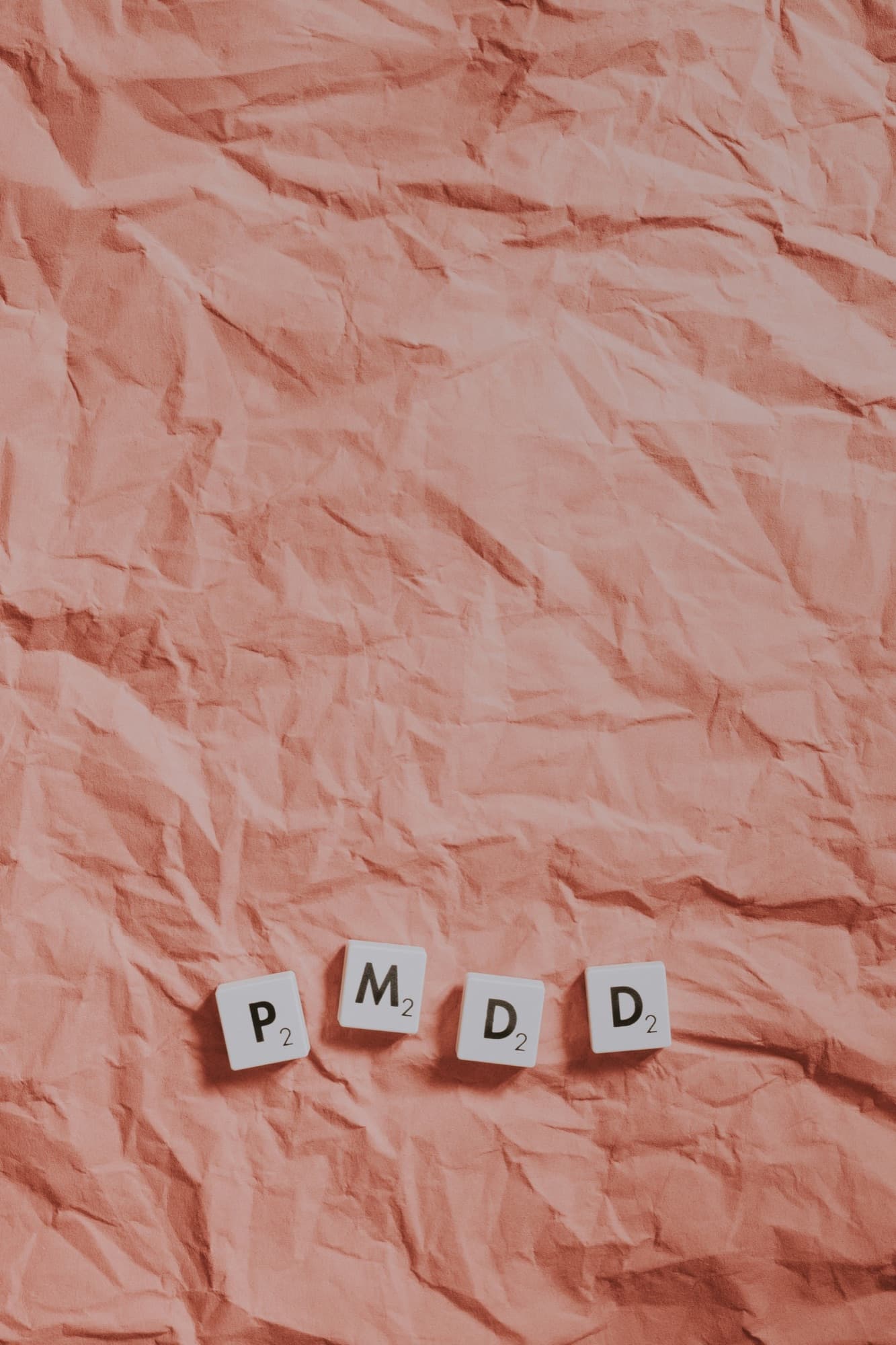 PMDD spelled out in Scrabble tiles on crumpled pink paper