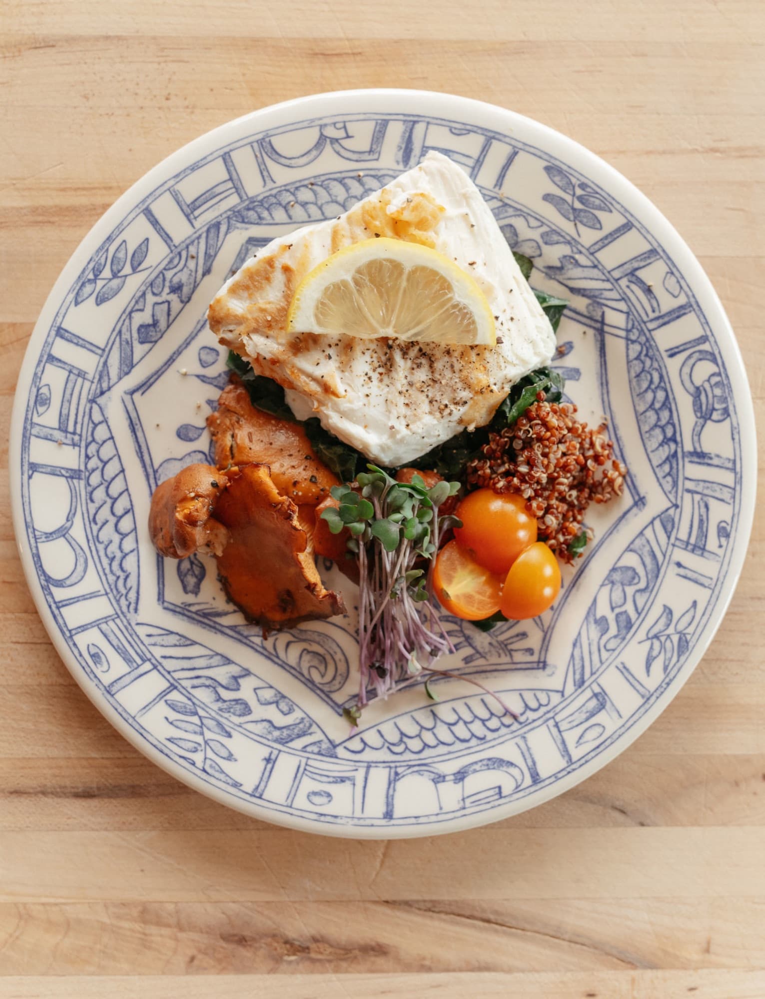 Pan-seared halibut with chanterelles, kale, quinoa, and microgreens on a hand-painted plate