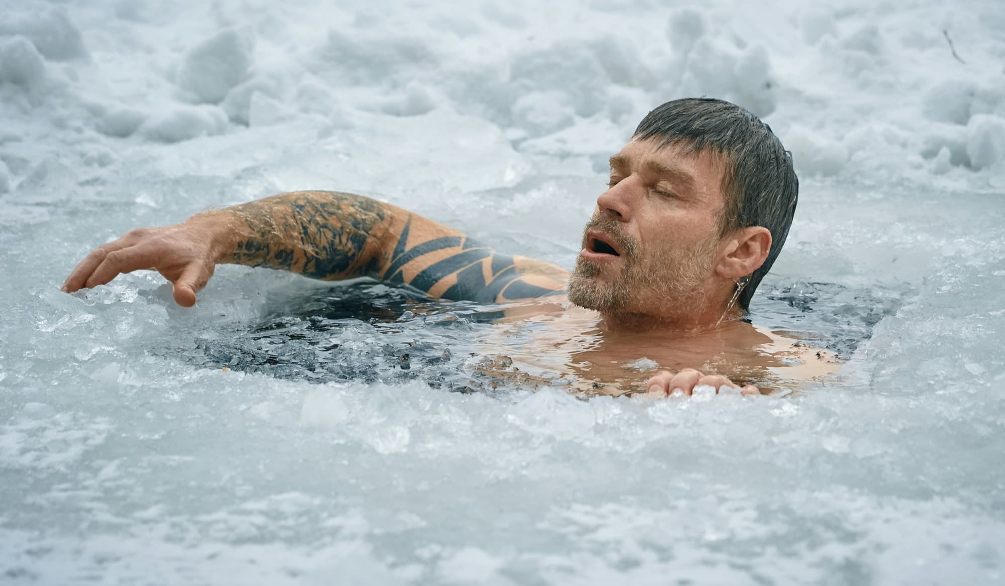 Tattooed man submerged in an ice bath, eyes closed